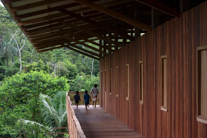 Covered exterior corridor with vertical timber cladding and patterned railing as children run through dappled light