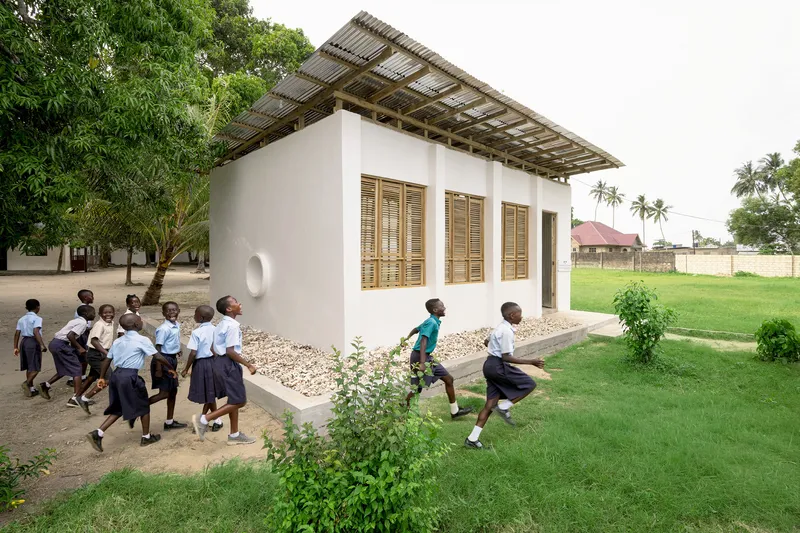White plastered classroom with louvered timber windows and corrugated metal canopy as children run past