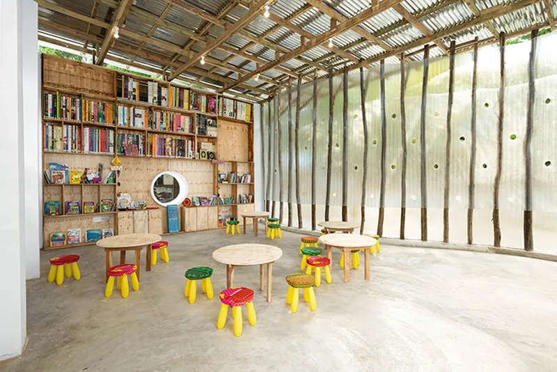 Library interior with plywood shelving along one wall and low tables on polished concrete floor
