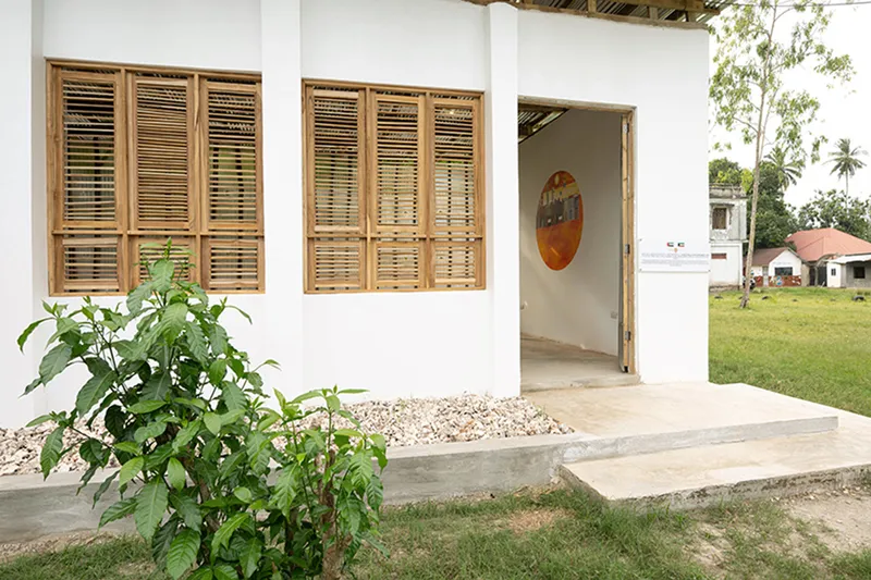 Entrance porch with louvered timber windows and gravel bed beside a planted shrub in grass