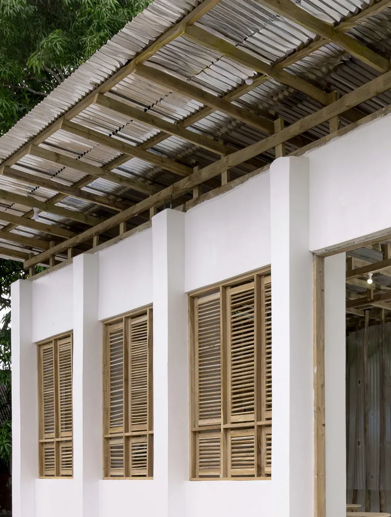 White wall with timber-framed louvered shutters beneath an open timber and corrugated metal roof structure