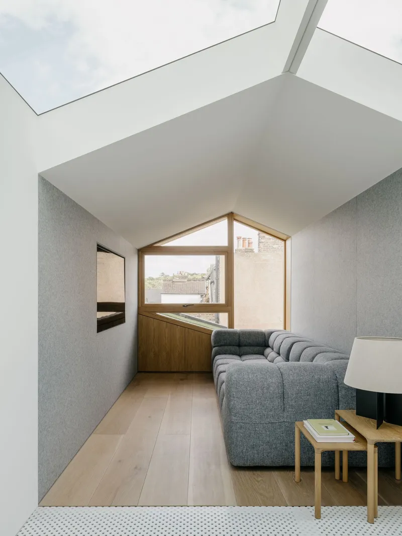 Gabled window framing rooftops beyond a living room with grey sofa and skylight above