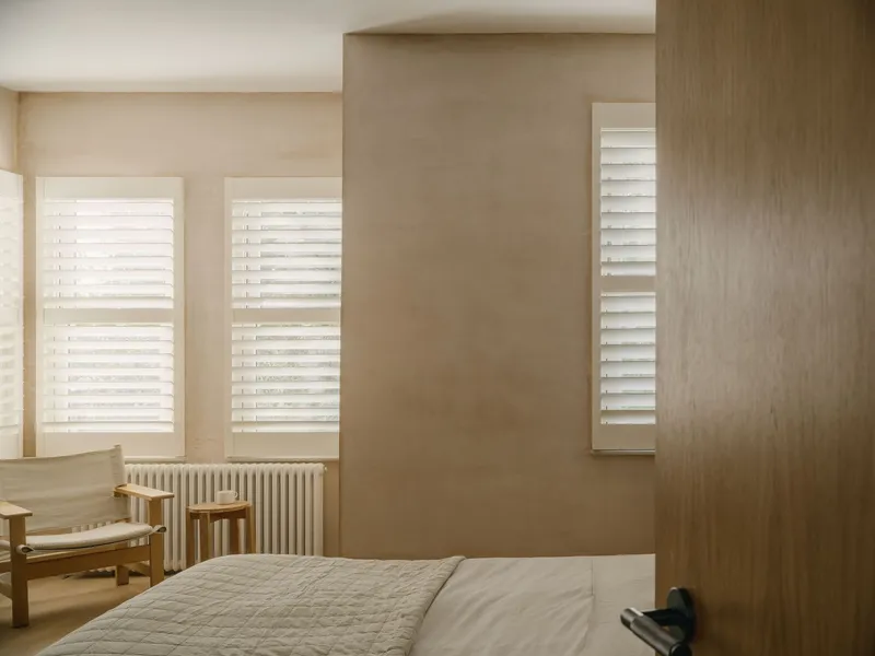 Bedroom with plywood wall panels and three windows fitted with white horizontal louvre blinds