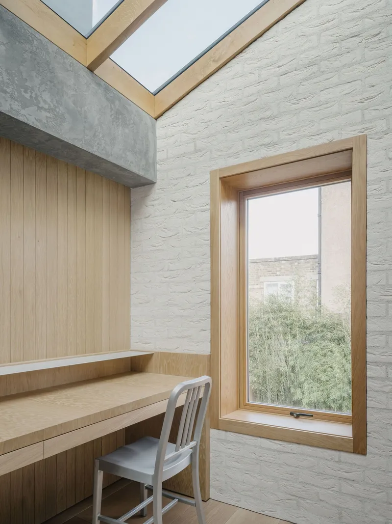 Study nook with built-in timber desk and painted brick wall beneath an angled skylight
