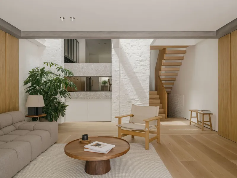 Double-height living space with curved timber staircase and white brick wall under natural daylight