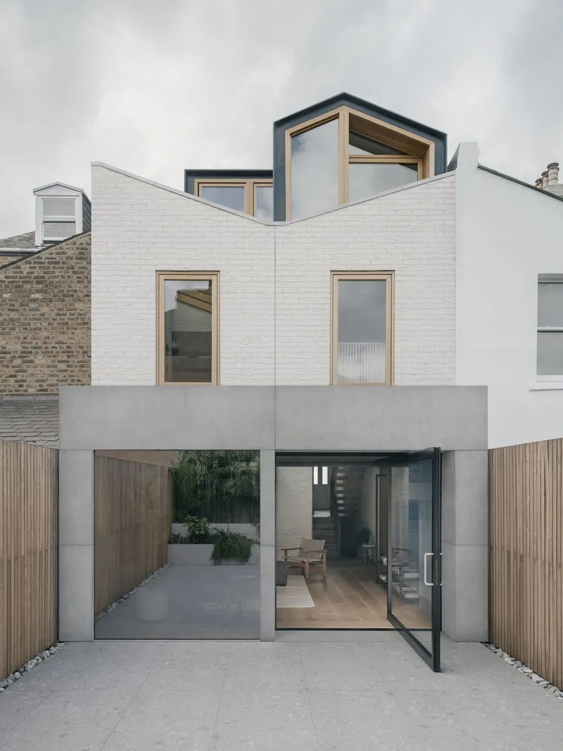Painted white brick facade with timber-framed windows and glazed courtyard entrance under overcast sky