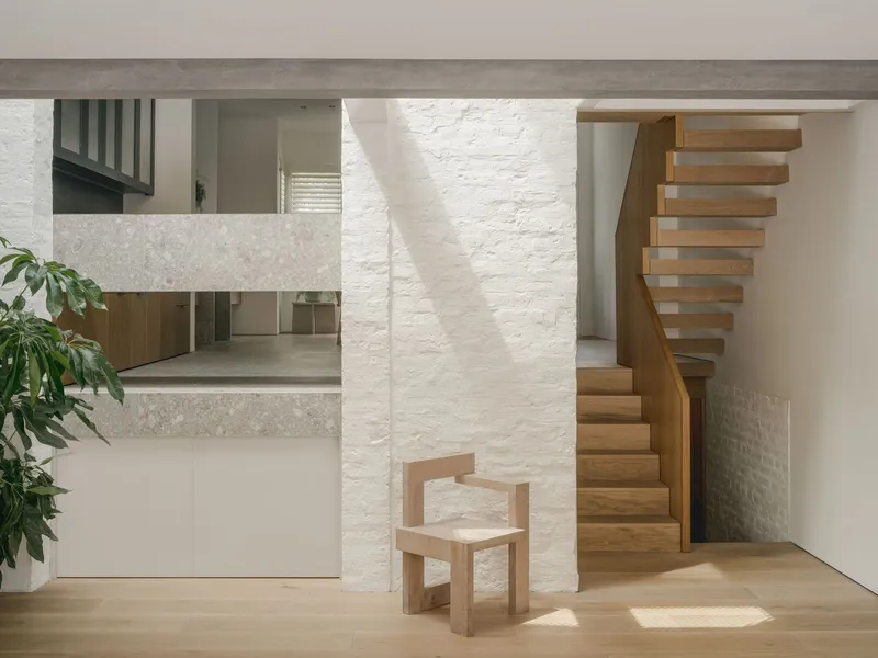 Curved timber staircase beside a painted brick column with afternoon sunlight on timber flooring