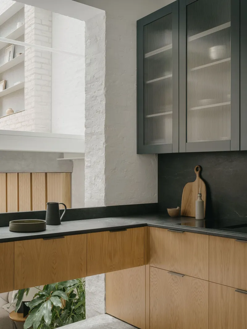 Kitchen corner with light oak cabinetry, black stone countertop and white textured plaster walls