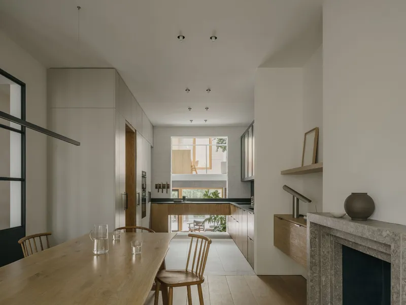Double-height dining room with timber table and steel-framed glass partition looking onto a courtyard