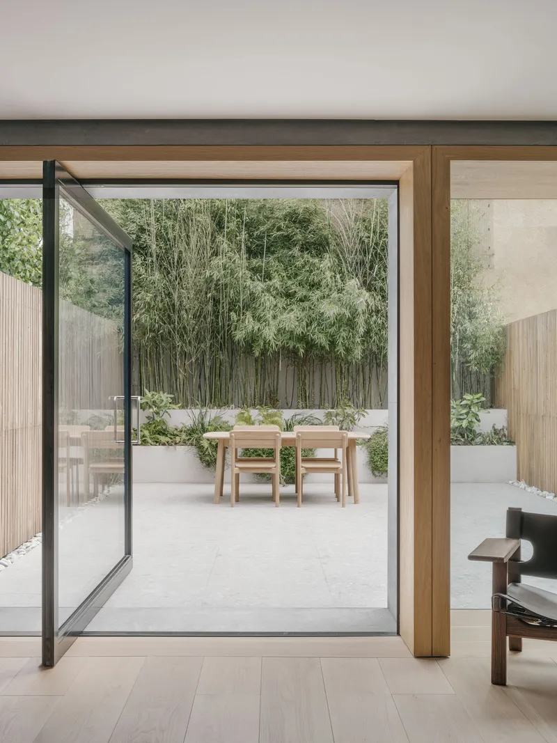 Pivoting steel-framed glass door opening onto a paved courtyard with bamboo and planted beds