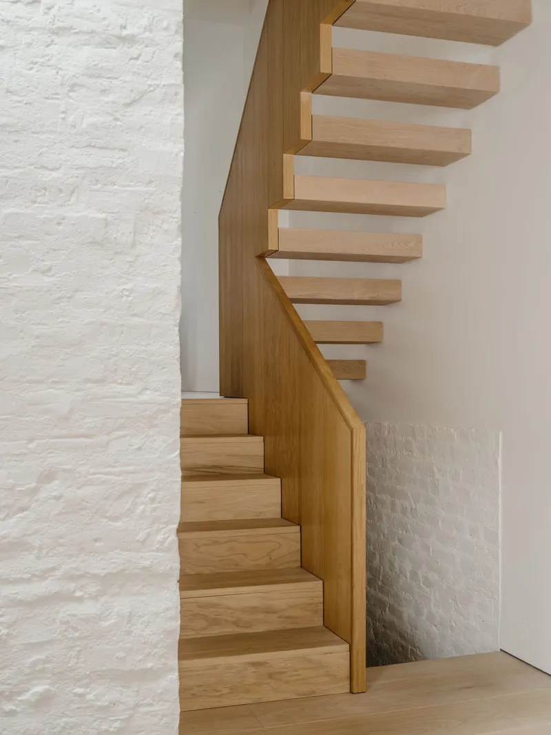 Close-up of the timber staircase turning against a white painted brick wall
