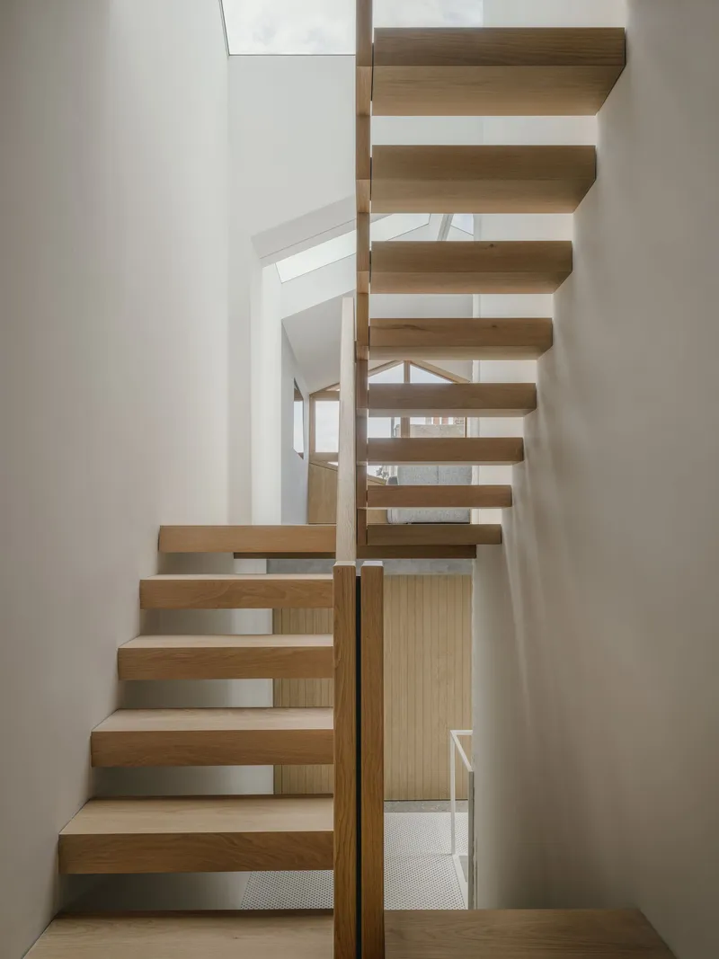 Timber staircase with cantilevered treads and vertical slat balustrade in a white-walled interior