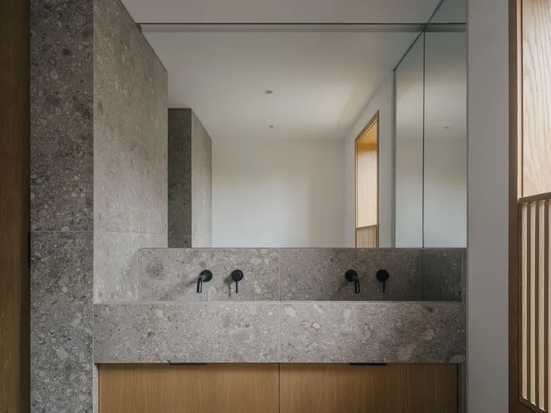 Double vanity with grey limestone and timber cabinetry beneath a full-width mirror in a bathroom