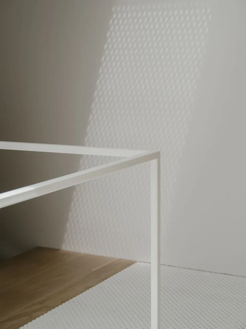 White painted staircase railing with textured mesh shadow cast on the wall by afternoon sunlight