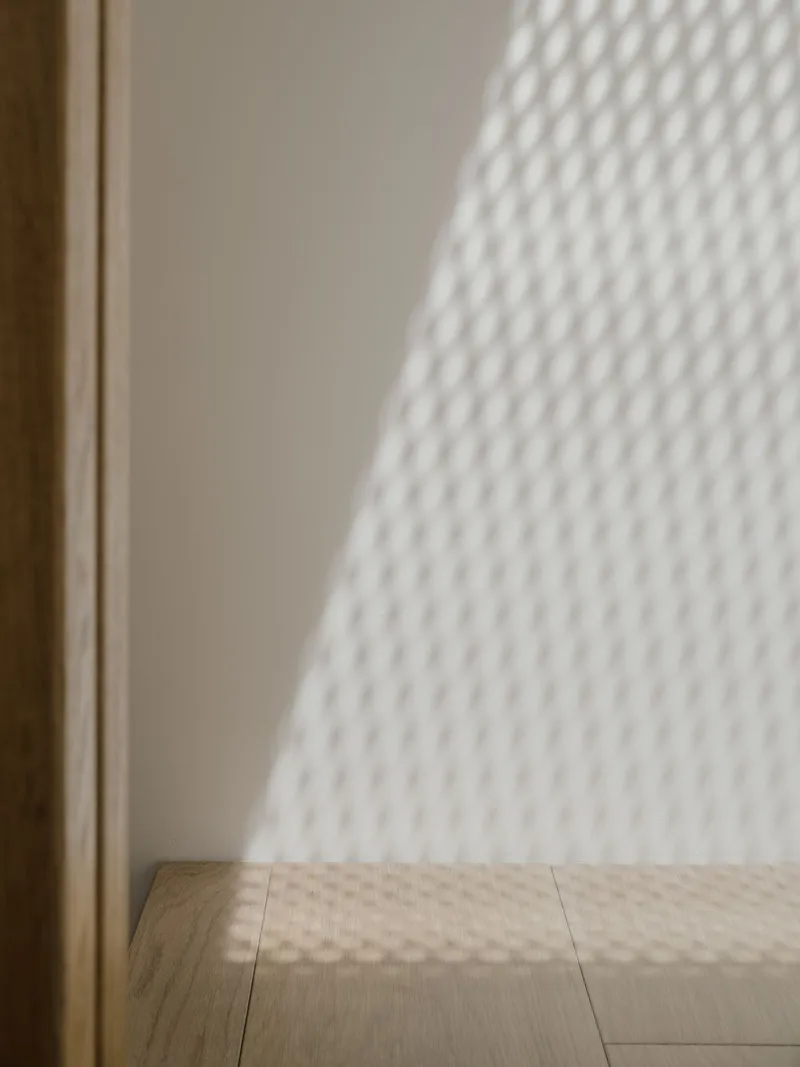 Corner junction where timber floor meets white painted wall beneath filtered window shadow pattern