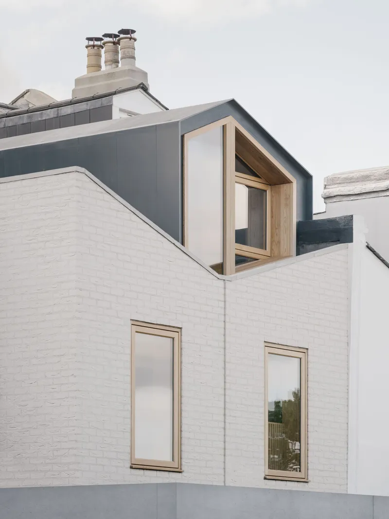 Timber-framed dormer window projecting from dark grey zinc roof above white painted brick facade