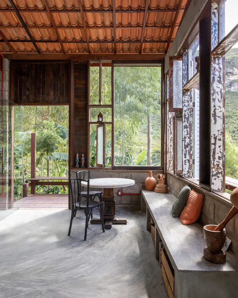 Interior dining nook with built-in concrete bench seating beneath timber-framed windows overlooking lush hillside vegetation