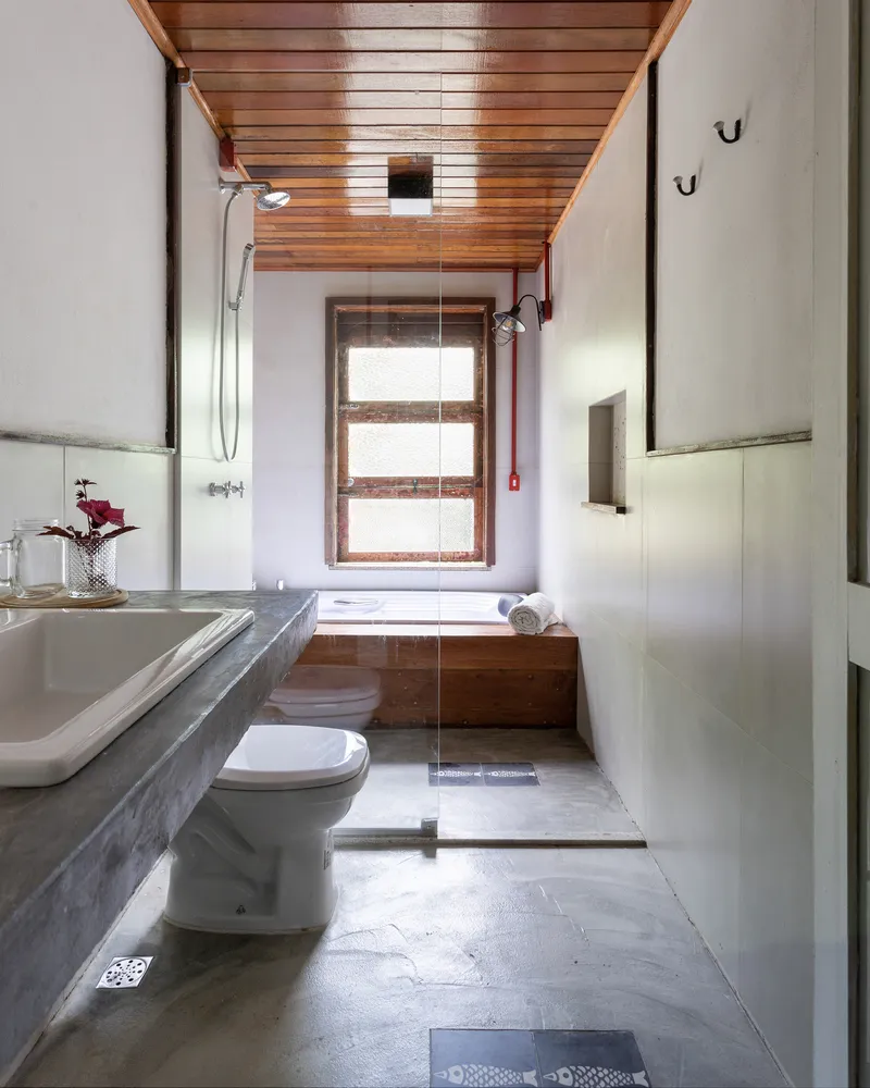 Bathroom with timber-clad tub beneath window, concrete floor and horizontal tongue-and-groove wood ceiling