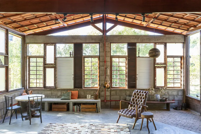 Living space with exposed timber roof structure, concrete block walls and grid windows overlooking greenery