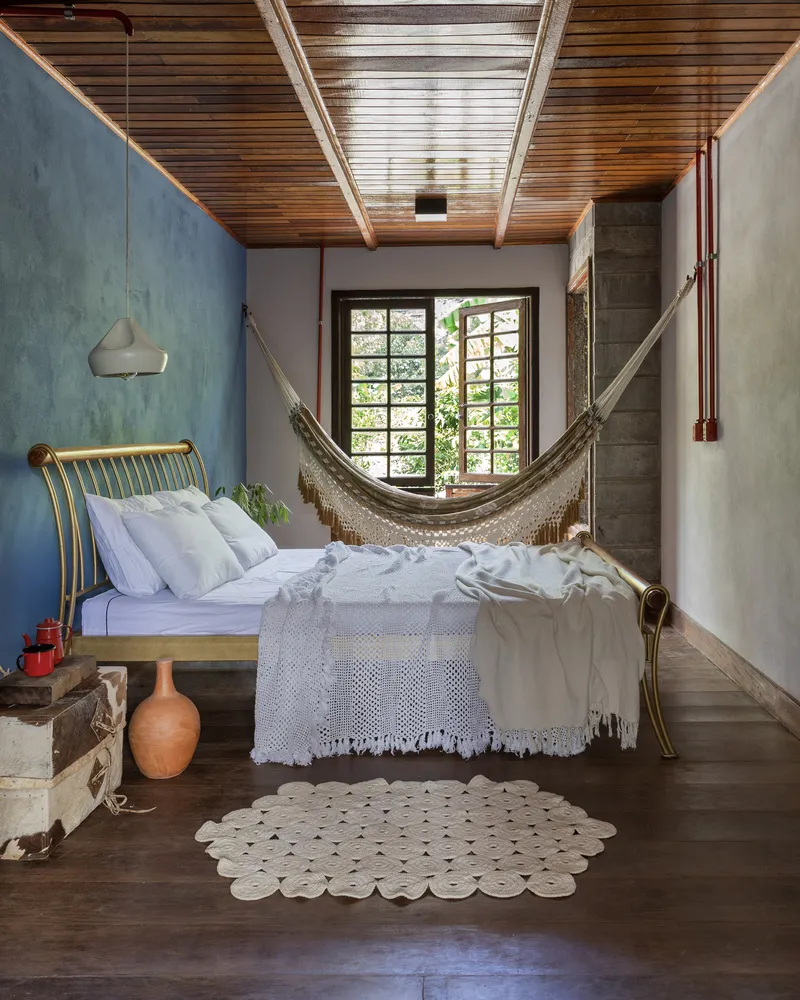Bedroom with timber plank ceiling, hammock and gridded window framing vegetation outside