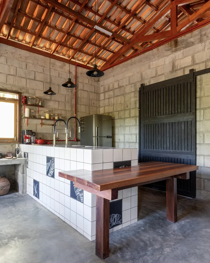 Kitchen island with white tile base, timber countertop and exposed clay tile roof above concrete walls