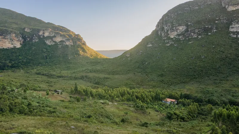 Valley landscape showing a low residence nestled among pine trees between two green mountainsides at dusk