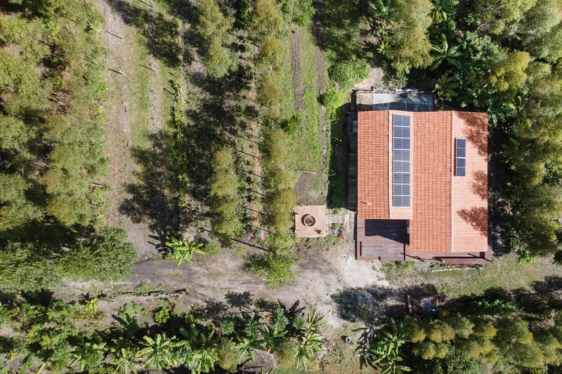 Aerial view of a brick and solar panel roof surrounded by forest clearing and scattered vegetation