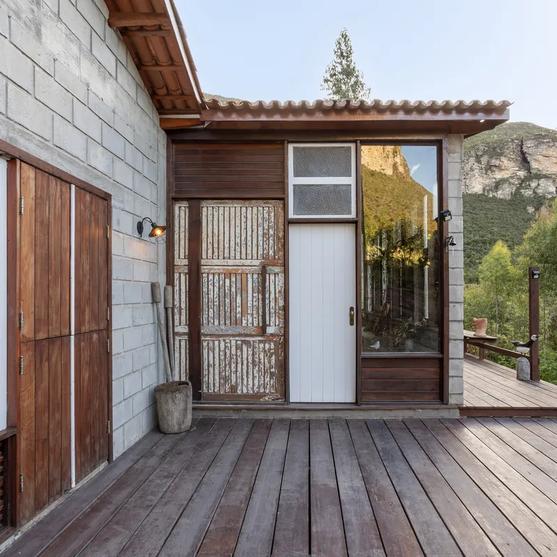 Entrance detail with corrugated metal panel and timber doors on a decked terrace overlooking distant cliffs