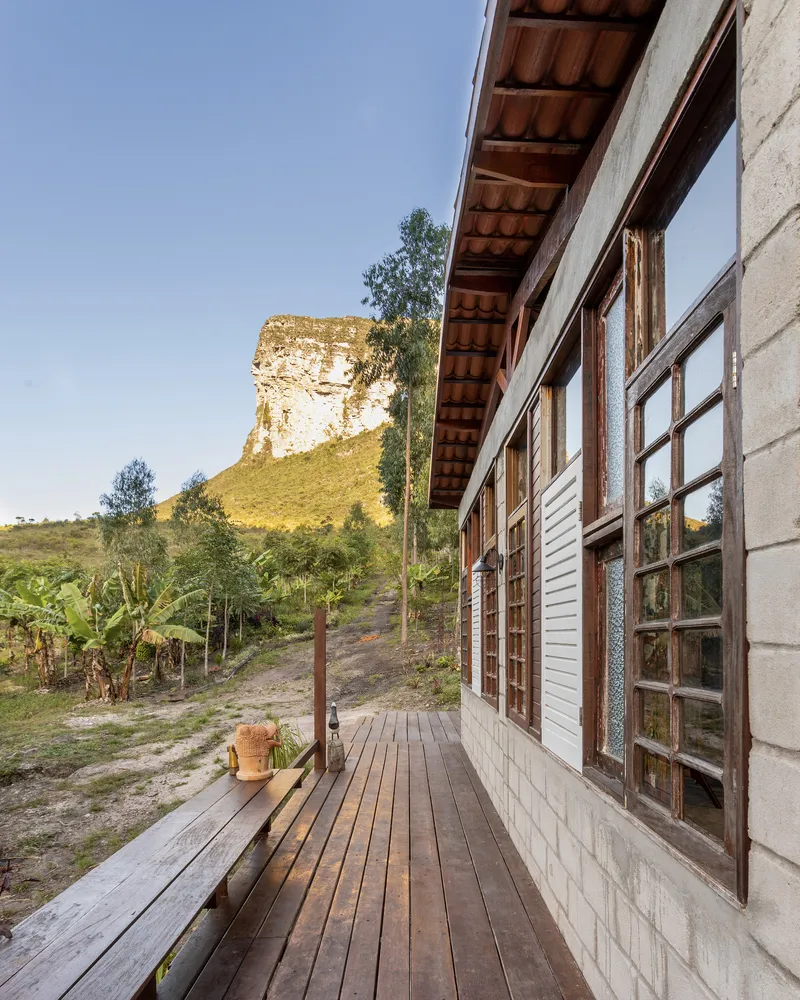 Timber deck veranda with clay tile roof extending along concrete block wall beneath a distant hilltop ruin