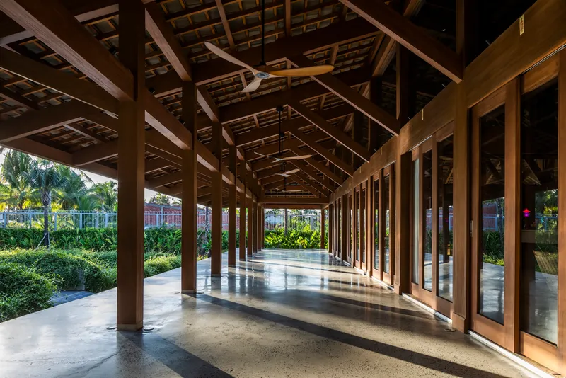 Covered timber colonnade with polished concrete floor and garden views filtering sunlight through columns