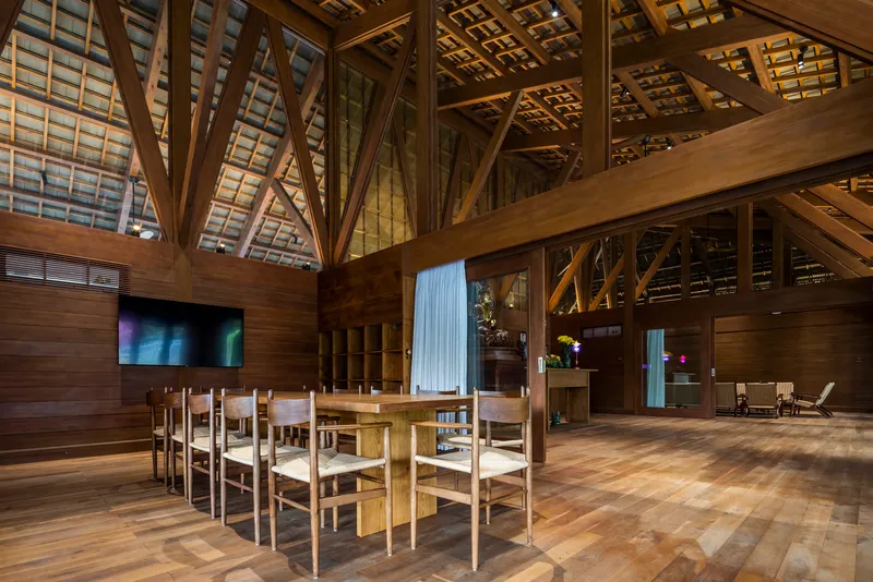 Dining area with timber chairs beneath diagonal braced roof trusses and wood-paneled walls