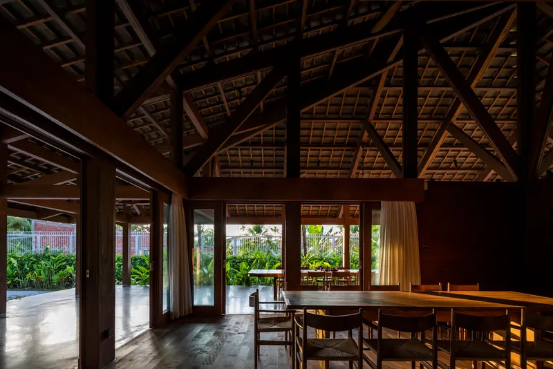 Dining space beneath exposed timber roof trusses with afternoon light filtering through glazed doors