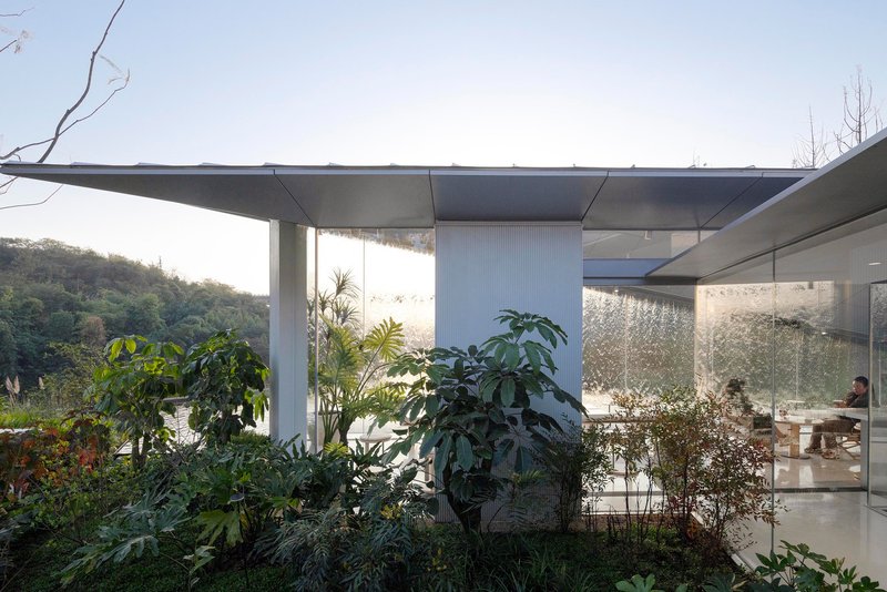 Glass-enclosed interior space with planted courtyard garden visible through floor-to-ceiling windows beneath deep concrete roof overhang