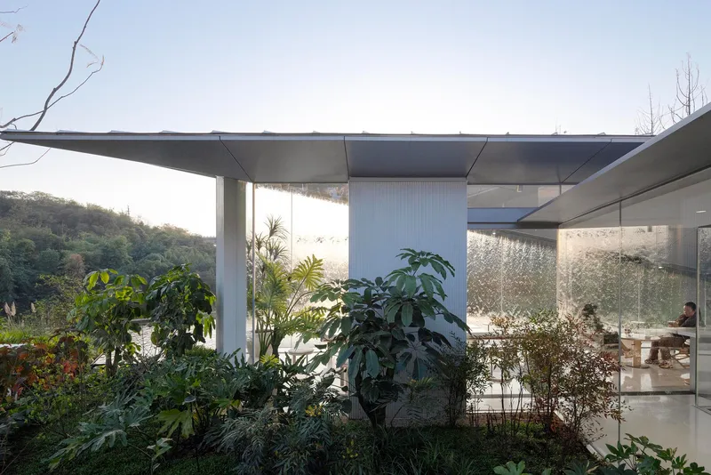 Glass-enclosed interior space with planted courtyard garden visible through floor-to-ceiling windows beneath deep concrete roof overhang