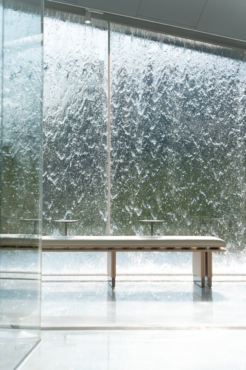 Interior view of a timber bench against floor-to-ceiling glass with cascading water feature outside