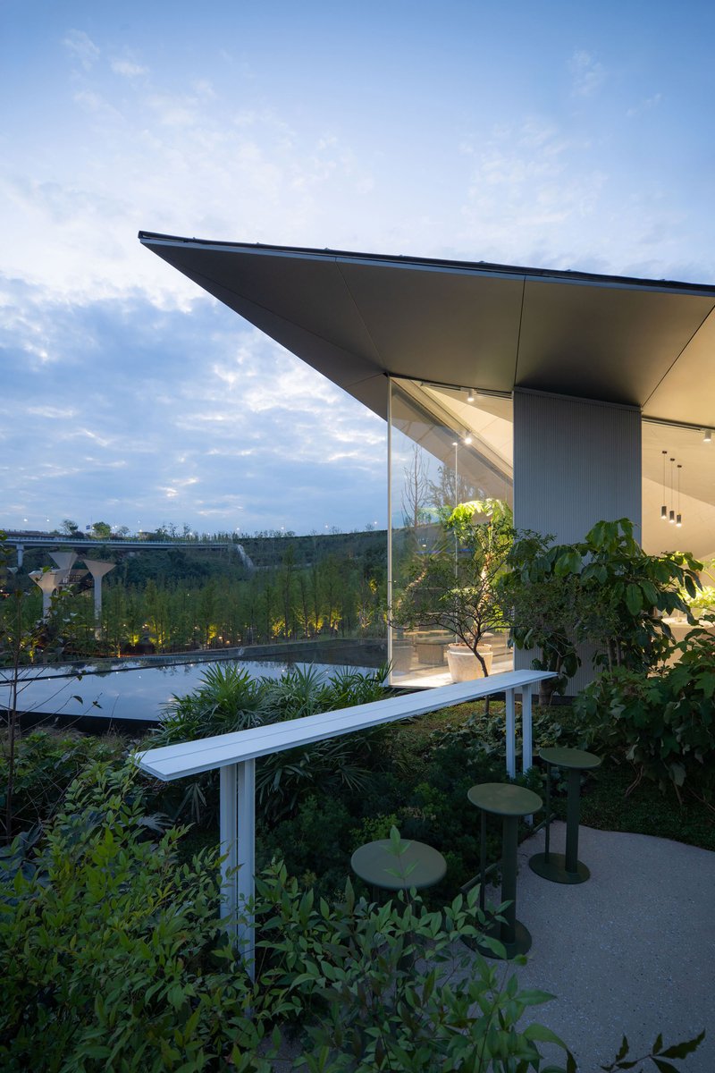 Covered terrace with cantilevered roof overlooking planted garden beds and water feature at dusk