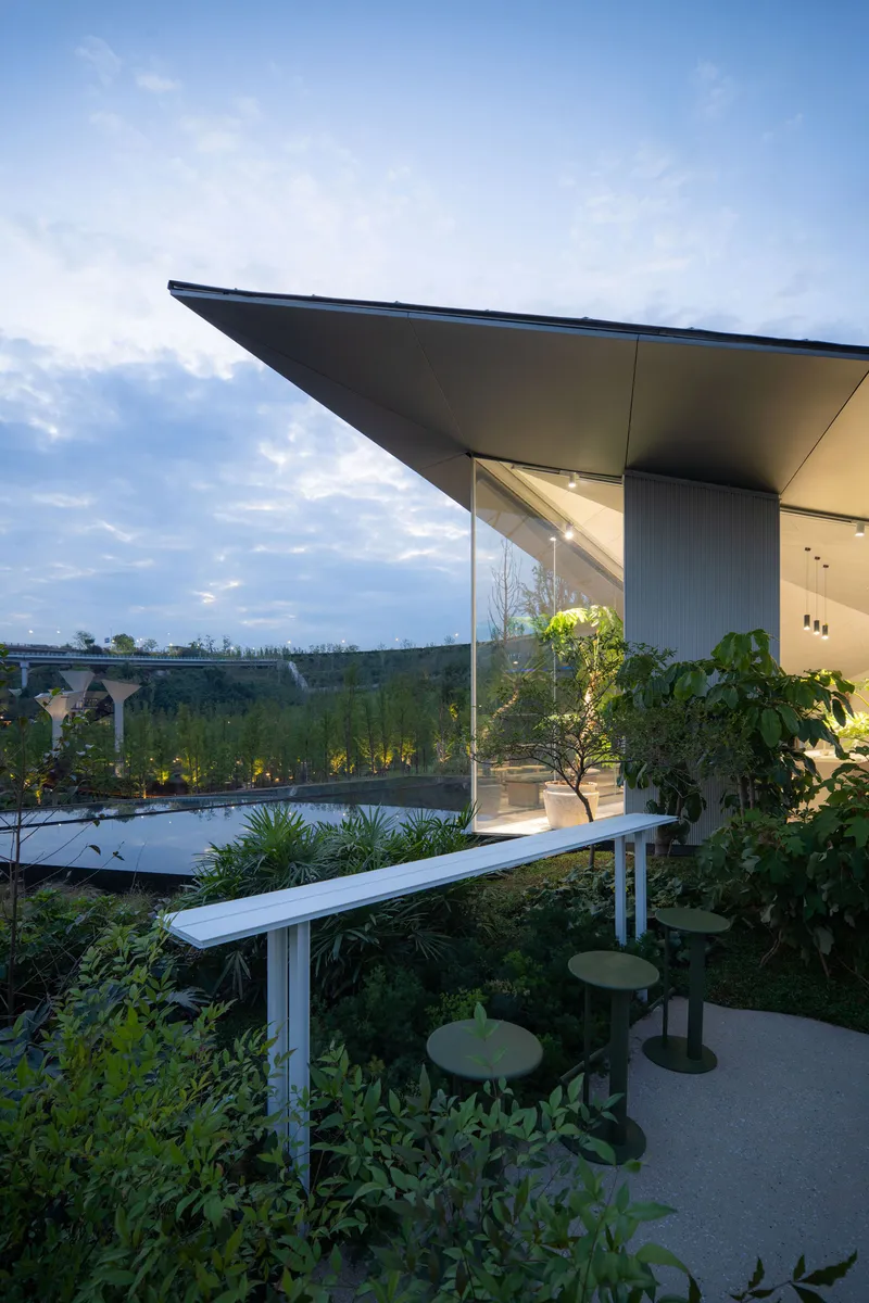 Covered terrace with cantilevered roof overlooking planted garden beds and water feature at dusk