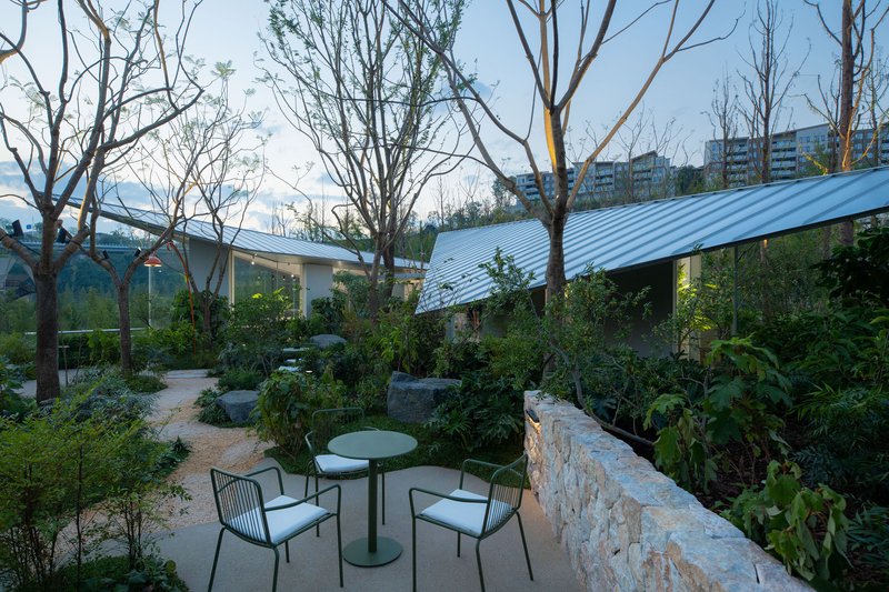 Courtyard seating area with stone retaining wall and corrugated metal roof visible beyond leafless trees