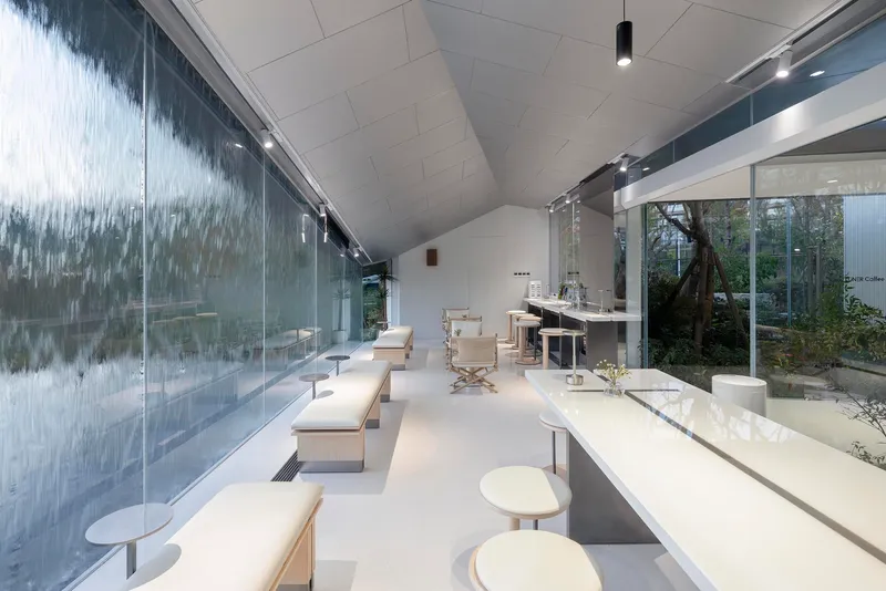 Interior gallery space with vaulted ceiling and textured glass wall reflecting adjacent garden