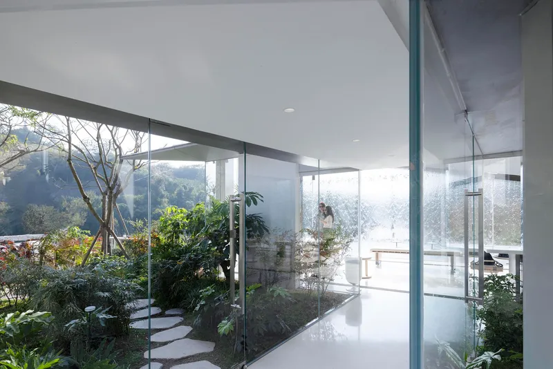 Interior circulation space with floor-to-ceiling glazing overlooking planted courtyard and stepped pathway