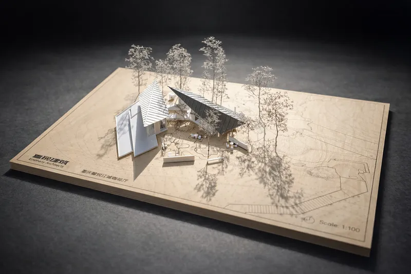 Physical model on plywood base showing angular roof volumes with miniature trees casting shadows
