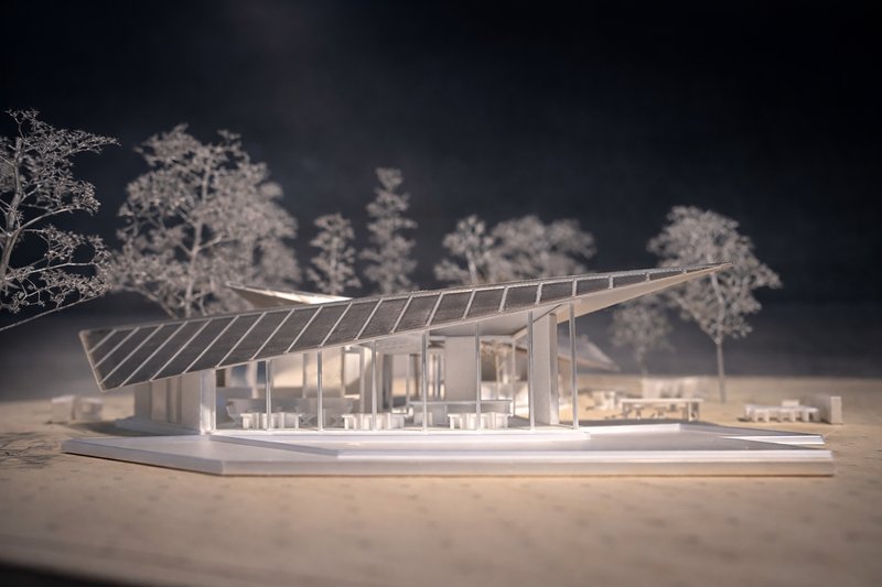 Physical model with illuminated interior showing the sloped roof and structural columns amid miniature trees