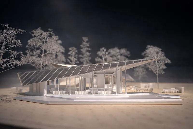Physical model with illuminated interior showing the sloped roof and structural columns amid miniature trees