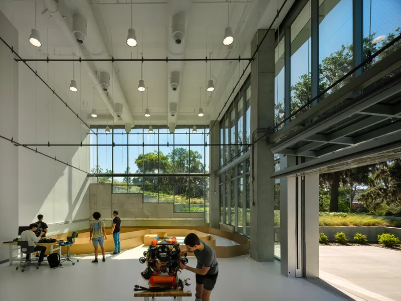 Double-height workshop space with exposed concrete columns and pendant lights overlooking a tiered seating platform