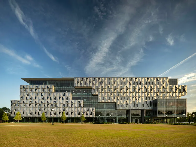 Long view of the facade with geometric precast panels and glass curtain wall across an open lawn