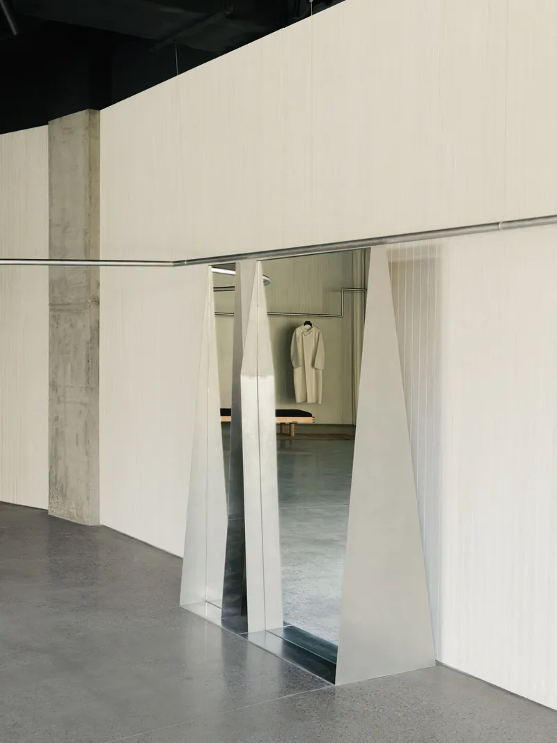 Curved wall opening with splayed metal frame revealing glimpse of hanging garment in next room