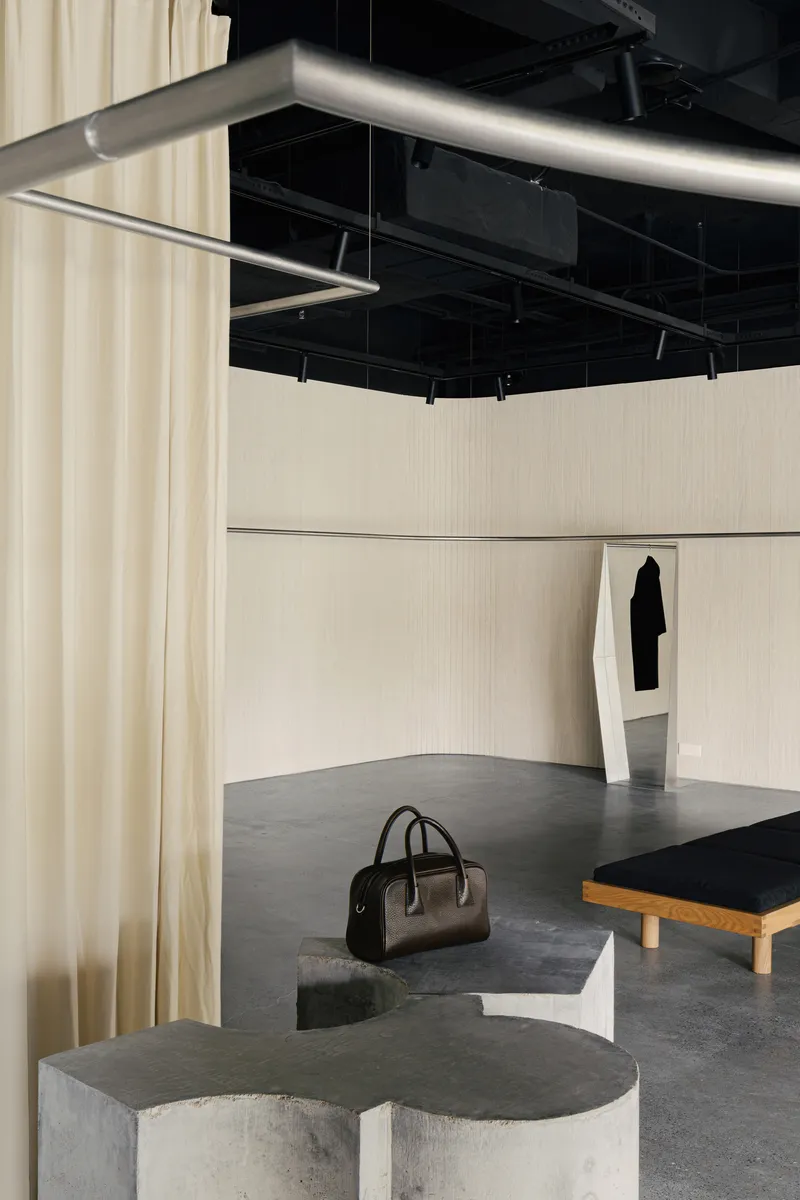 Curved concrete seating plinth with darkened top beneath suspended steel clothing rails and track lighting