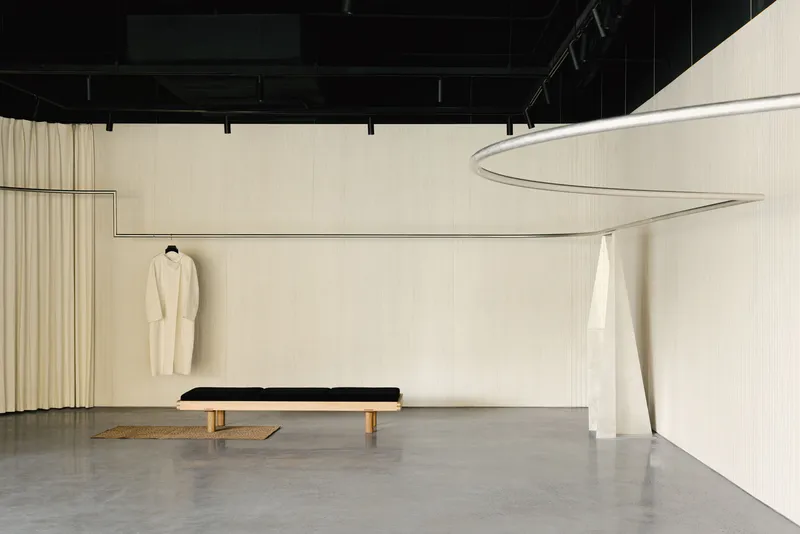 Pale curved wall with vertical ribbing beneath an exposed black industrial ceiling with track lighting
