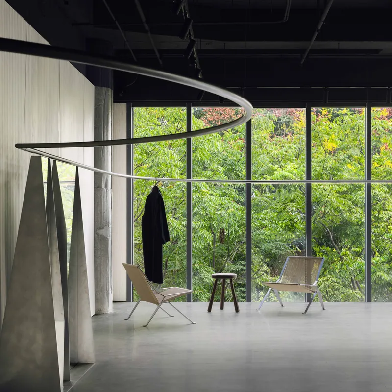 Full-height glazed wall framing a view of dense foliage with folding chairs and coat hooks below