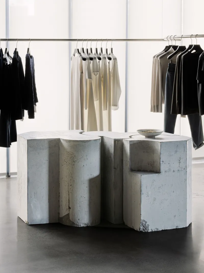 Cast concrete display counter with undulating faceted surfaces beneath hanging garments in a retail interior